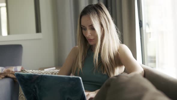 Concentrated Woman Sitting on Sofa Browsing Social Media on Laptop