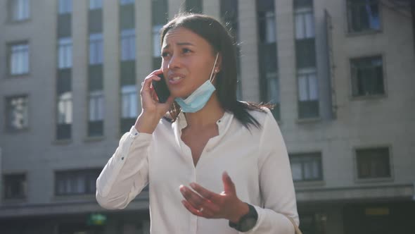 African american woman wearing face mask talking on smartphone in city street