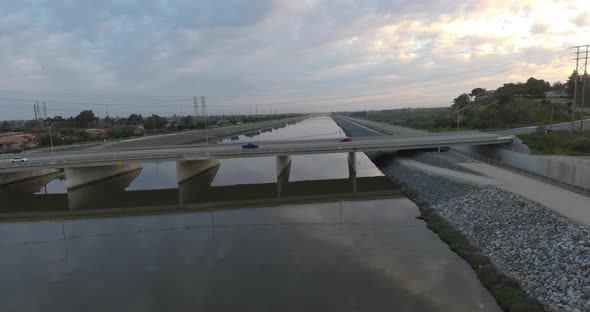 A drone glides sideways over a body of water as cars drive over a bridge.