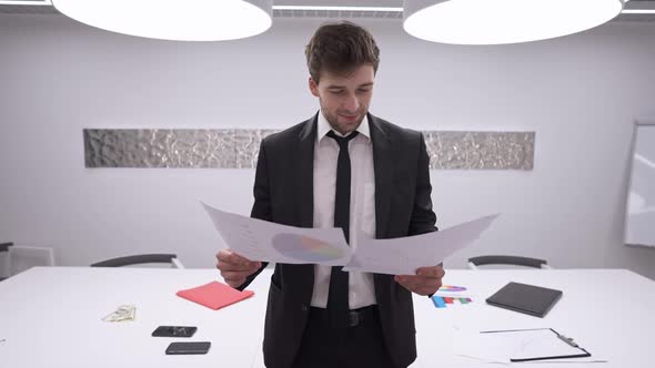 Medium Shot Portrait of Smiling Confident Successful Man Analyzing Documents Looking at Camera