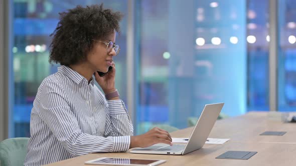 African Businesswoman with Laptop Talking on Smartphone in Office 