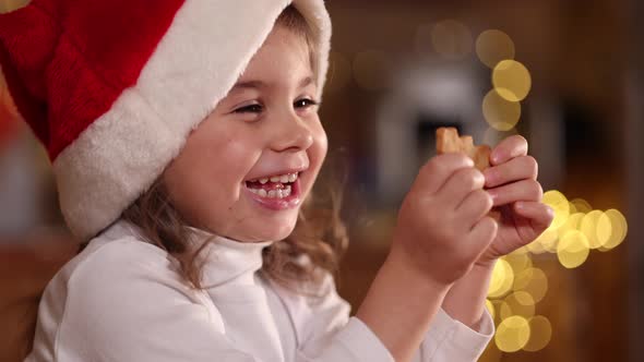 Adorable Little Girl in Santa Hat Eating Homemade Gingerbread and Laughing