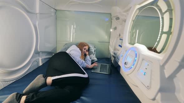 A Girl is Resting in a Pod Hotel Capsule with a Laptop