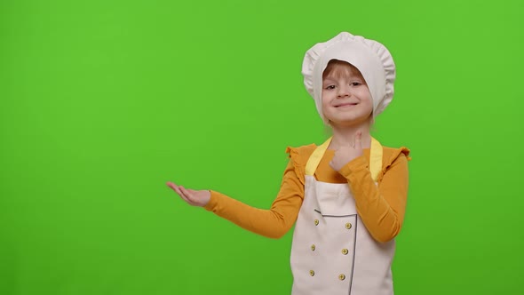 Child Girl Dressed Like Chef Cook Pointing at Left on Blank Space Place for Your Advertisement Logo