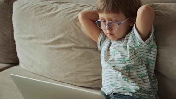 Child Watching Video and Using Laptop Sitting on Sofa at Home