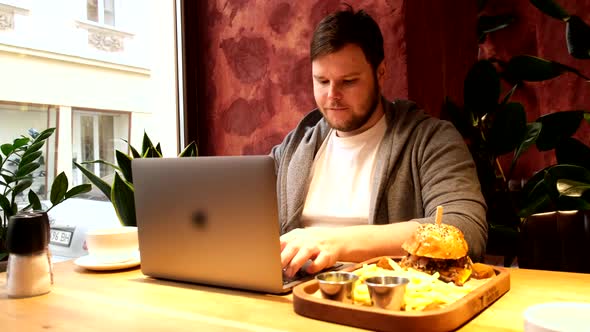 Man Working on Laptop in Cafe Eating Burger