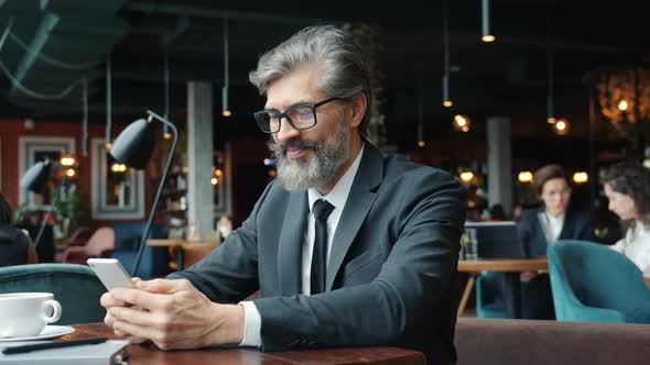 Handsome Mature Man in Suit Using Smart Phone Texting in Restaurant Alone