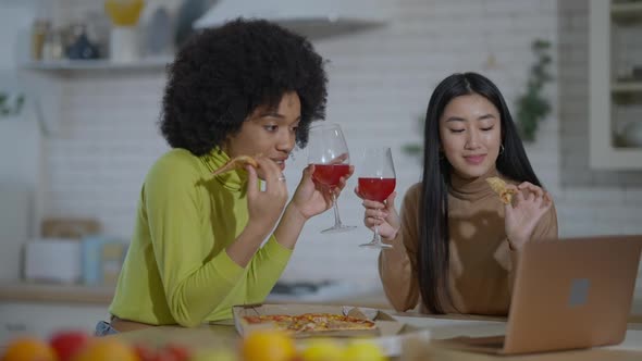 Two Slim Beautiful Multiethnic Women Eating Pizza Drinking Wine Using Social Media on Laptop