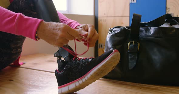 Senior woman tying shoelace in gym changing room 4k