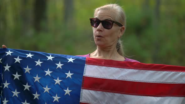 Closeup of pretty, blonde woman holding up an American flag and showing surprise and excitement.