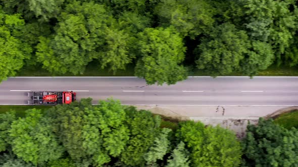 Lorries from above - driving fast over a straight street in a forest, filmed by travcking the heavy