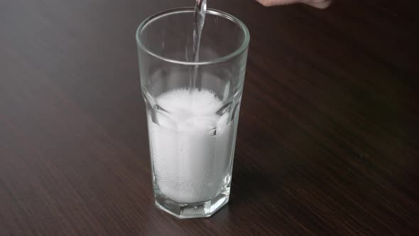 Pouring transparent soda into a tall glass on a wooden table