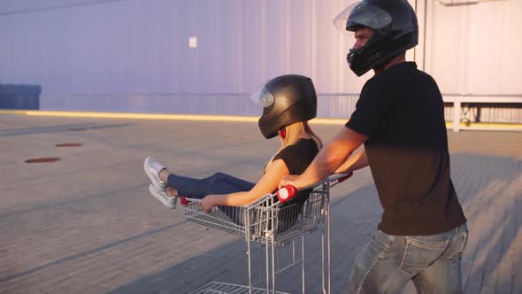 Guy Rolls Attractive Young Woman in the Trolley in Motorcycle Helmets at Sunset