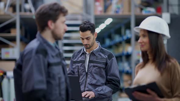 Concentrated Busy Handsome Middle Eastern Man Typing on Laptop Keyboard in Warehouse As Blurred