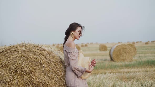 Stylish Lady Wore in Dress in Sunglasses   Posing at a Haystack in a Windy Field