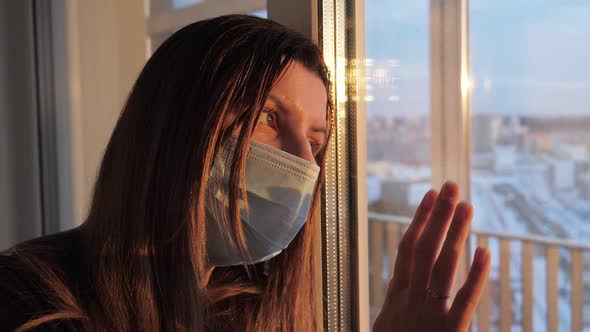 Sadness Caucasian Woman In Mask Looks Hopefully Out Window At Sunset Light