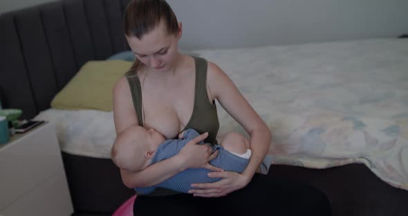 Young Mother Lulls and Breastfeeds Her Little Baby Boy on a Fitball in Bedroom