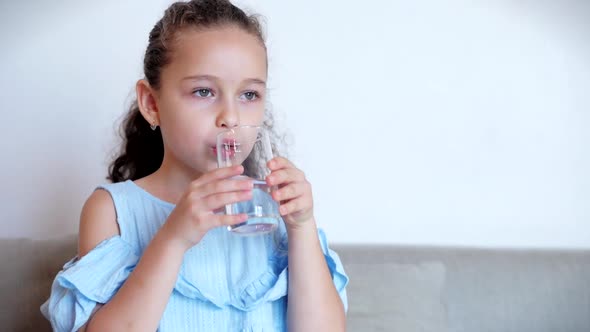 Cute Baby Girl Drinking a Glass of Water Sitting on the Couch at Home. Slow Motion Little Boy