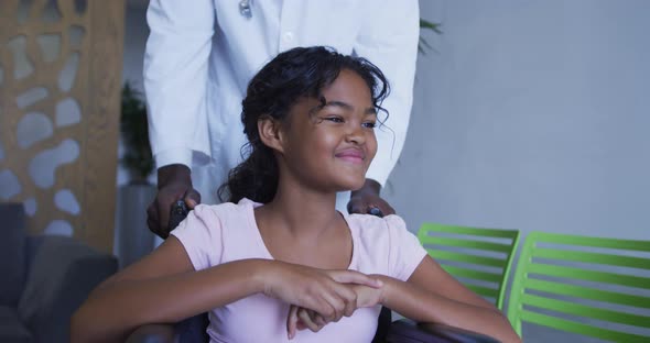 Mid section of doctor pushing smiling african american girl in wheelchair at hospital