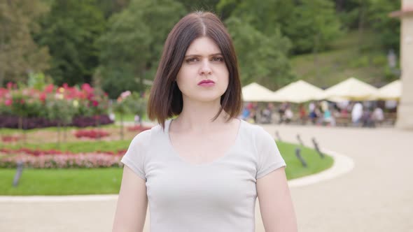 A Young Caucasian Woman Shows a Thumb Down to the Camera and Shakes Her Head in a City Park