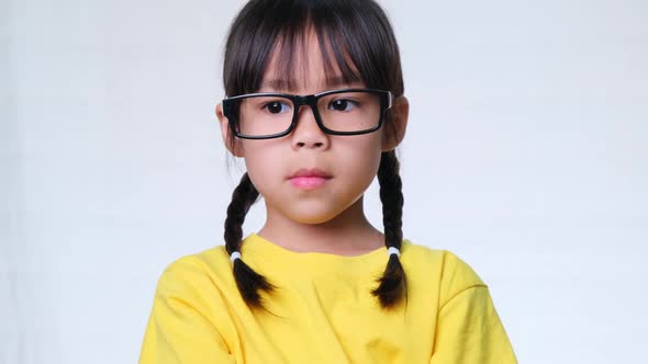 Angry girl with glasses and a yellow t-shirt stands with her arms crossed against a white background