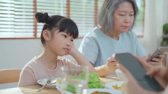 Upset daughter sitting at lunch table looking to addicted parents using smartphones while eating.