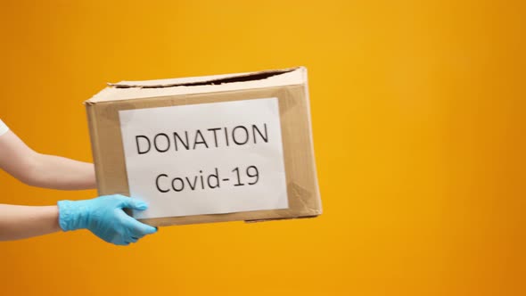 Human Hands Holding Cardboard Box with Coronavirus Donations Against Yellow Background