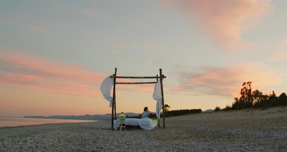 Young girl sleeps in a canopy bed at sunset on the beach near the ocean