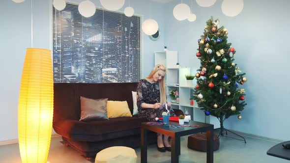 Beautiful Woman Writing Letter on Christmas Sitting on Sofa Near the Xmas Tree