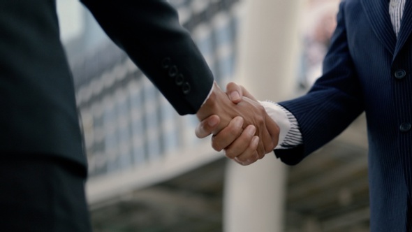 Asian businessman and businesswoman shaking hands partnership deal business while standing outside.