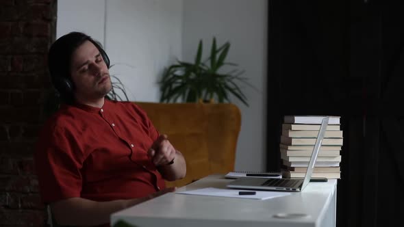 Man working at home office at laptop and listen a music in headphones