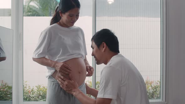 Young Asian Pregnant couple man kiss his wife belly talking with his child feeling happy smiling