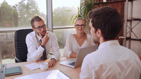 Male Job Applicant in White Shirt Speaking with Caucasian Boss in Glasses Sitting at Table with