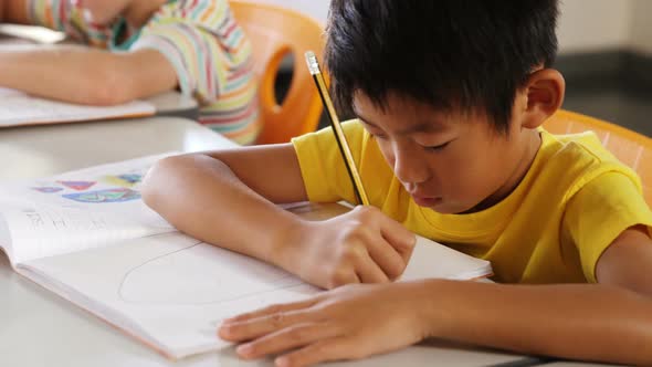 Schoolboy drawing in book in classroom