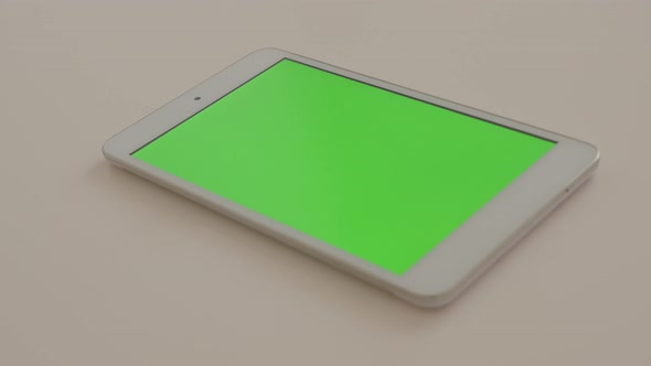 Silver PC tablet on white reflective background displaying green screen chroma 4K 2160p UltraHD foot