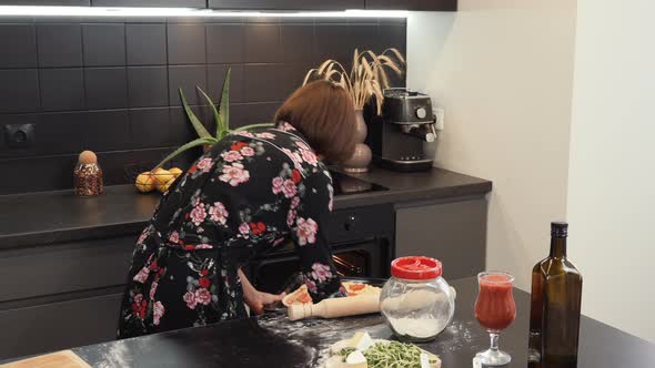 Woman putting homemade pizza in oven and closing door