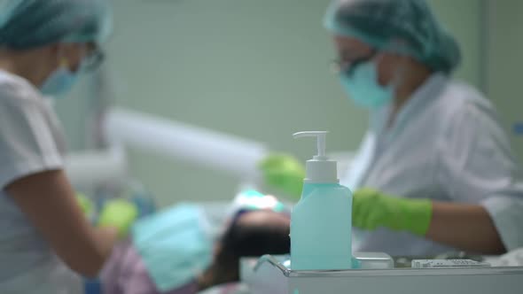 Disinfectant in Dental Office with Blurred Doctor and Assistant Curing Patient at Background