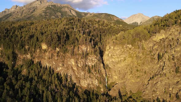 Aerial rising over Corbata Blanca thaw waterfall between mountains and pine tree woods at golden hou