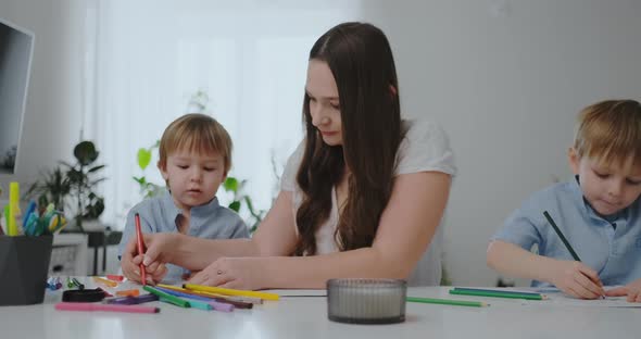 Sitting at the Table in the Living Room, a Young Mother Teaches Her Son To Hold a Pencil