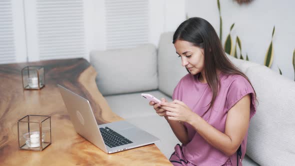 Woman Sitting at Table Using Laptop and Phone for Work in Cafe