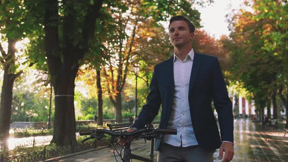 Handsome Young Man Walking with His Bicycle in Park in City Center During Sunrise Slow Motion