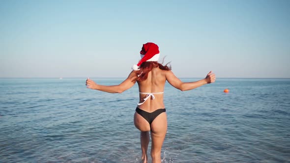 Woman in Swimsuit and Santa Claus Hat Runs Into Sea