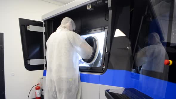 A Man in a White Protective Suit Stands Near a Large 3D Printer