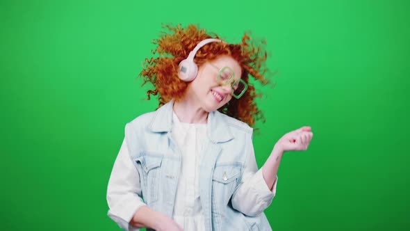 Young Happy Redhead Woman in Wireless Headphones Enjoying Music and Dancing Over Green Chroma Key