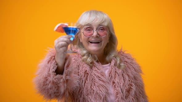 Cheerful Elderly Lady in Funny Pink Outfit Drinking Blue Cocktail, Age Positive