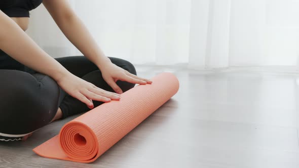 Woman wearing sportswear and roll the orange yoga mat.