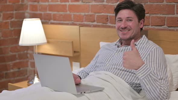 Middle Aged Man with Laptop showing Thumbs Up in Bed