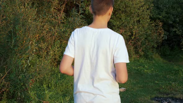 Unrecognizable Teenage Guy Throws a Plastic Bottle Into the Bushes View From the Back