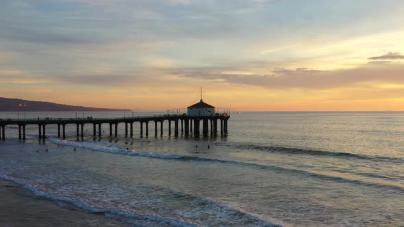 People Swim At The Manhattan Beach With Roundhouse Aquarium On Pier At Dusk. - aerial