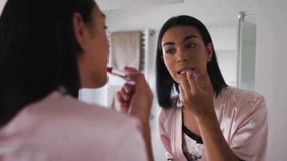 Mixed race gender fluid person standing in bathroom and using a lipstick